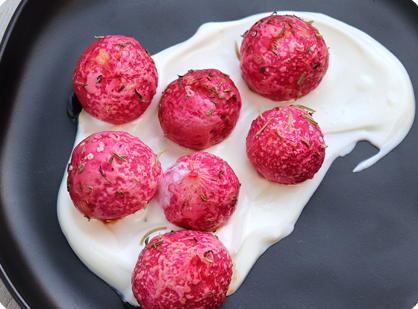 Seven roasted radishes on a pool of creamy white sauce all on a black plate..