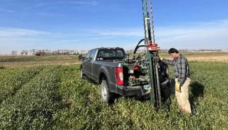On a clear fall day, a soil scientist stands alongside a soil sampling probe in a test plot.