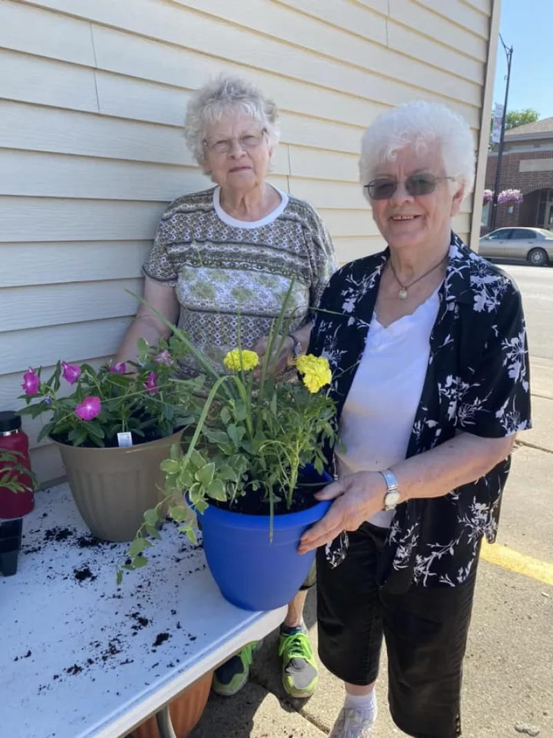 Two elderly women posing with the plants they potted