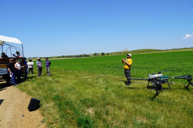 man speaks to a crowd about a drone (sitting behind him)