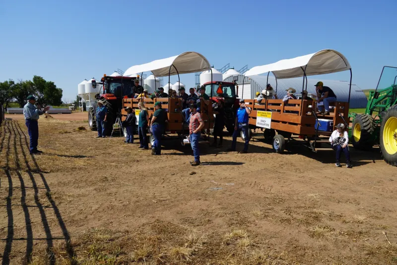 groups in wagons listen to a speaker in front of a pen
