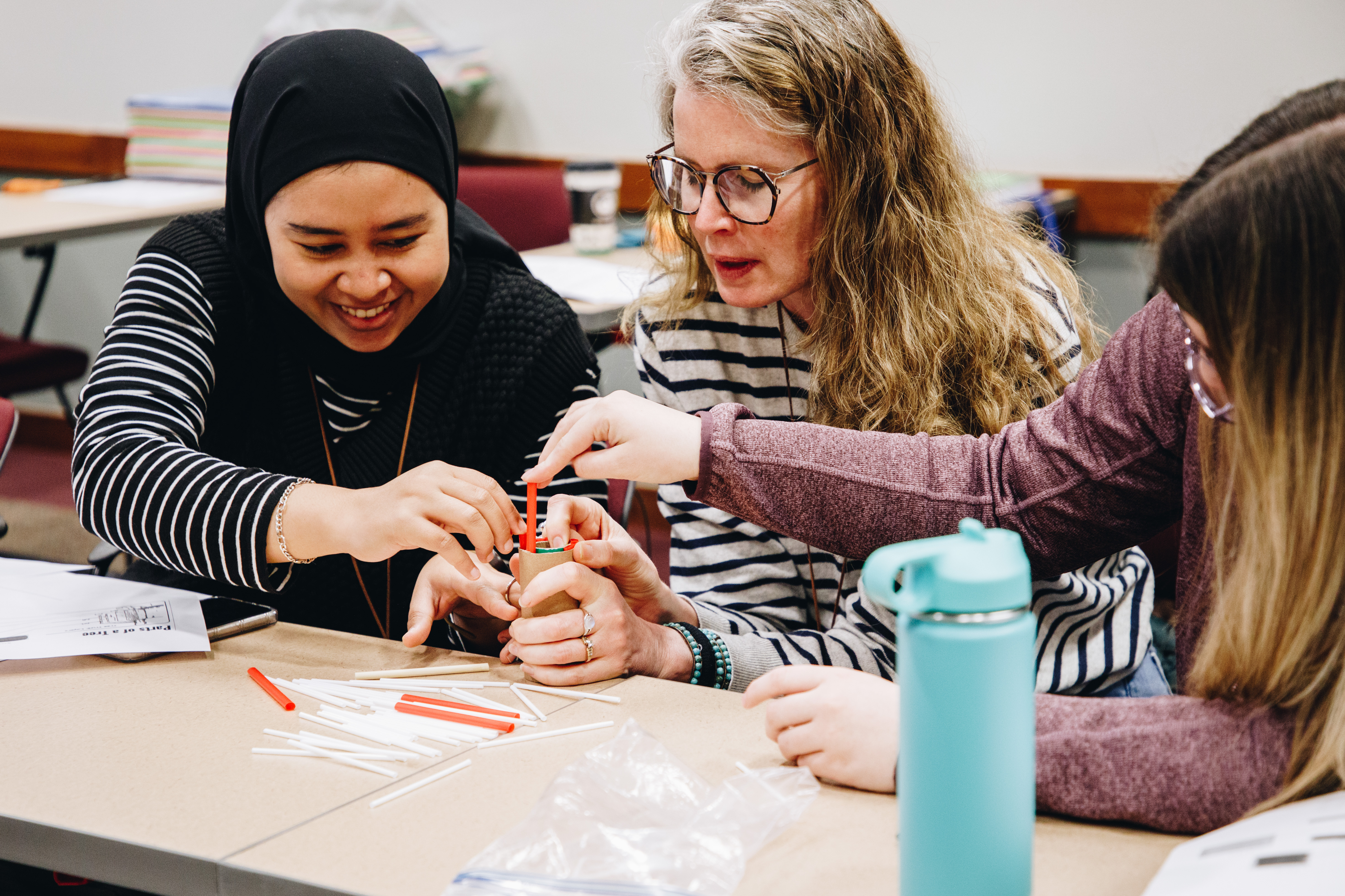 A group of women work together to put straws into a toilet paper roll to model the parts of a tree
