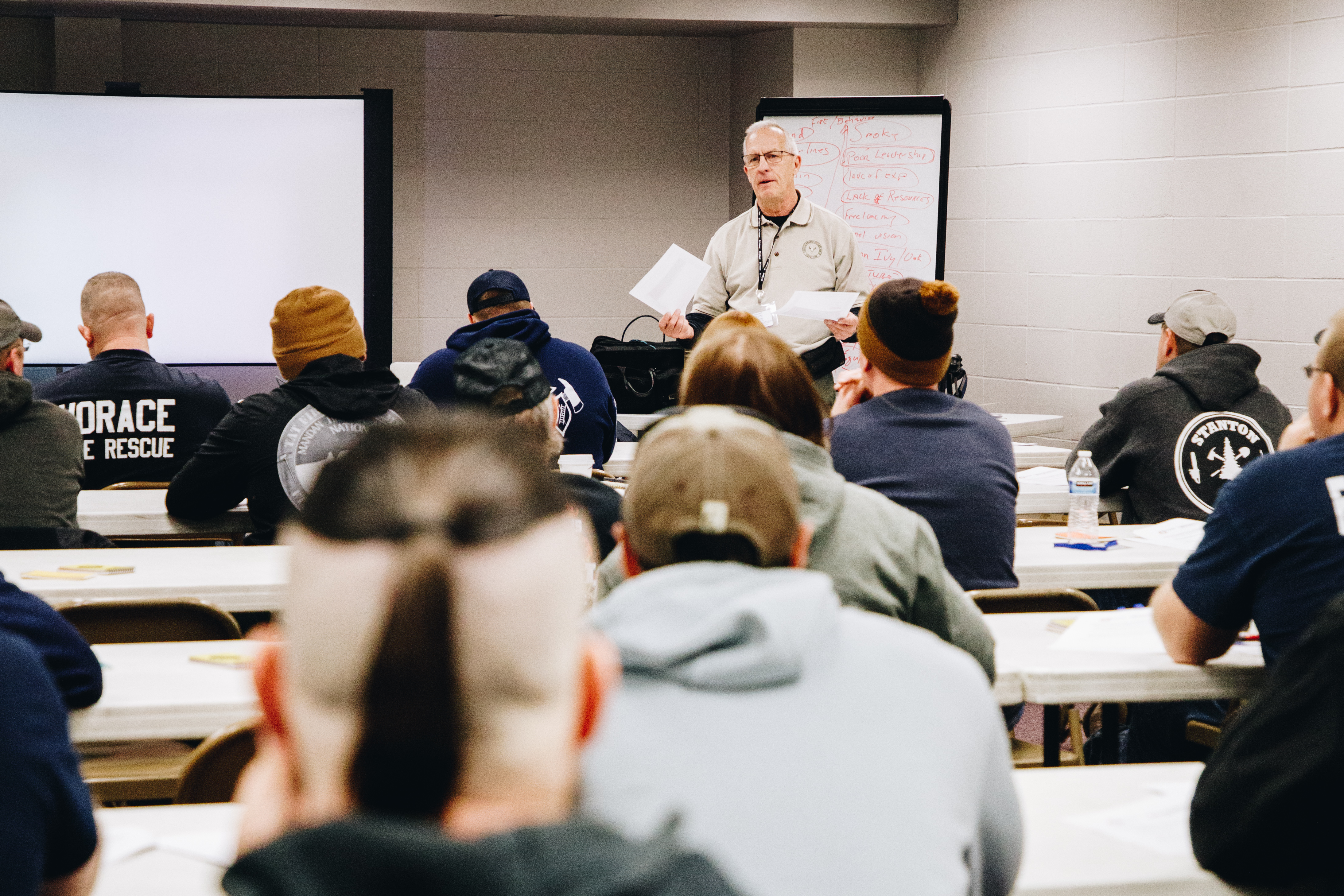 A man leads a class of firefighters sitting at tables