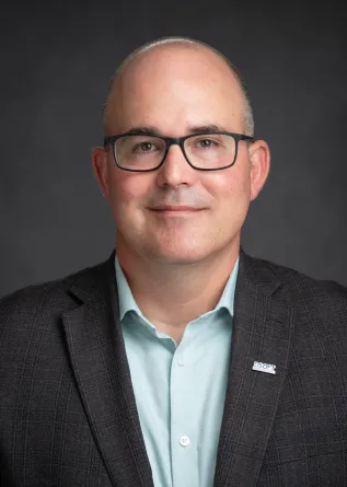 Head shot of Dr 安德鲁·b·克罗尔.  He wears a light green button up shirt with a dark sport coat.  He wears dark rimmed glasses and has very little hair on his head.