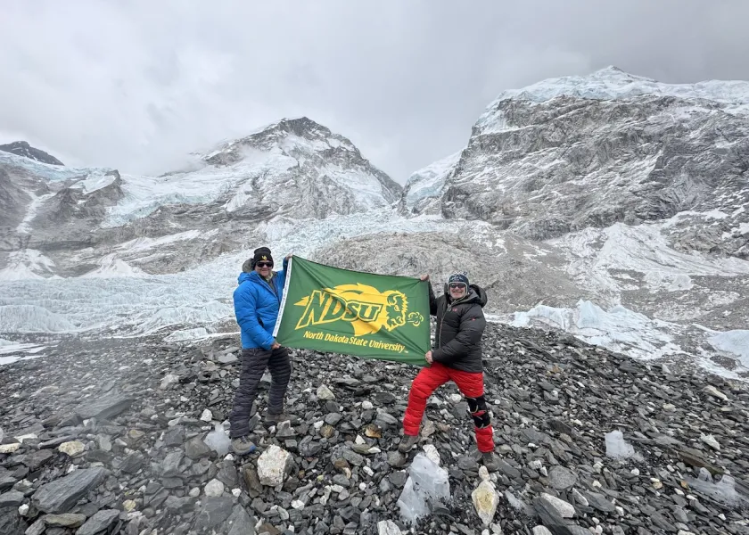 线上赌博app alum, Lee Hoedl pictured in red climbing pants, holds the 线上赌博app flag at the base of the Khumbu Icefall.