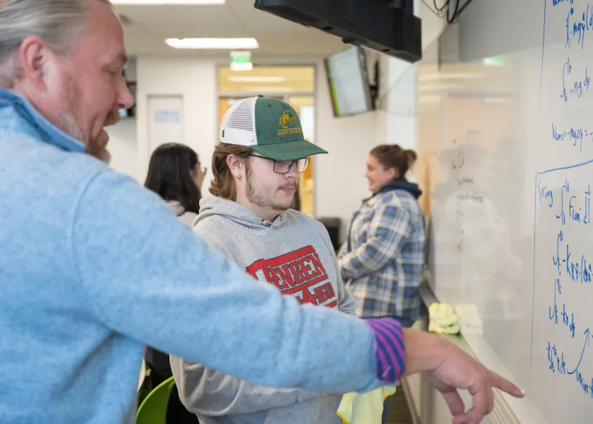 professor working with a student at a whiteboard