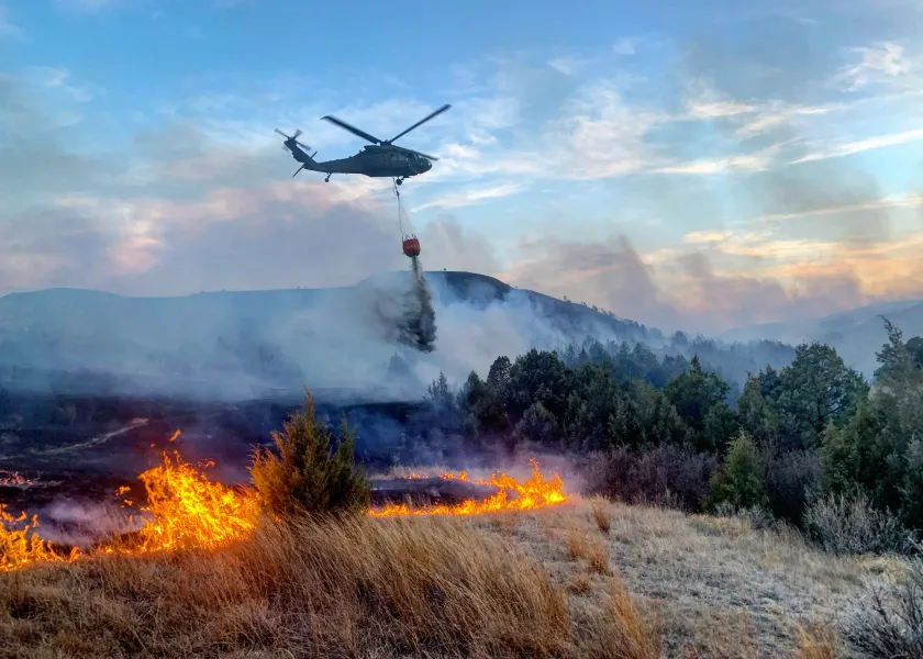 A Blackhawk helicopter drops water onto a fire burning near a forest