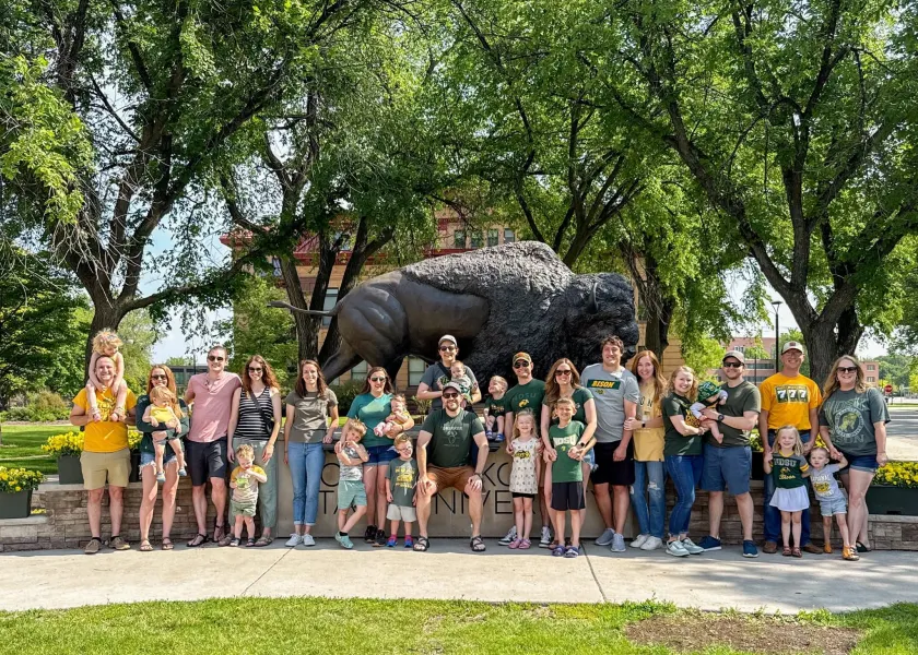 A group of 线上赌博app alum and friends stand in front of the Bison statue on 线上赌博app's campus.
