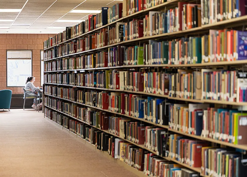 shelves full of books and a student studying in the library