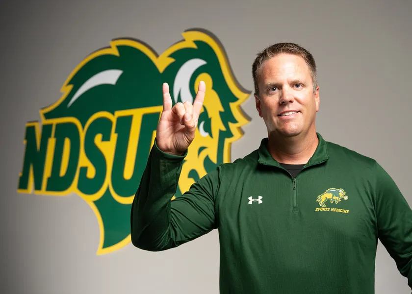 alumni Mike Kjellerson giving Bison horns and smiling in front of an 线上赌博app wall graphic