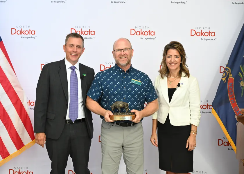 A man holds a bison-shaped award next to a man and woman