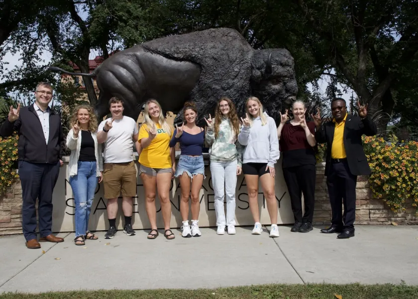 The six graduate students in 线上赌博app’s Center for Agricultural Policy and Trade Studies stand in front of the Bison statue. 