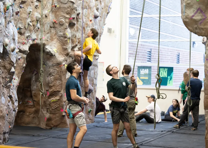 students checking equipment before using the rock climbing wall