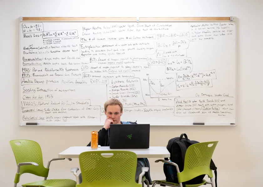 student using a laptop and the white board inside of a campus study space