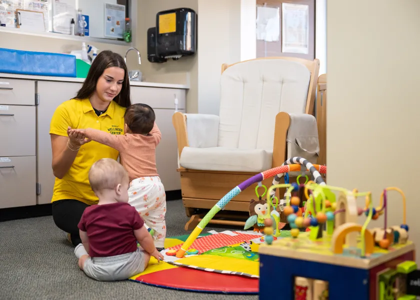 Femae student worker in child care playing with two infants in Wellness Center Child Care