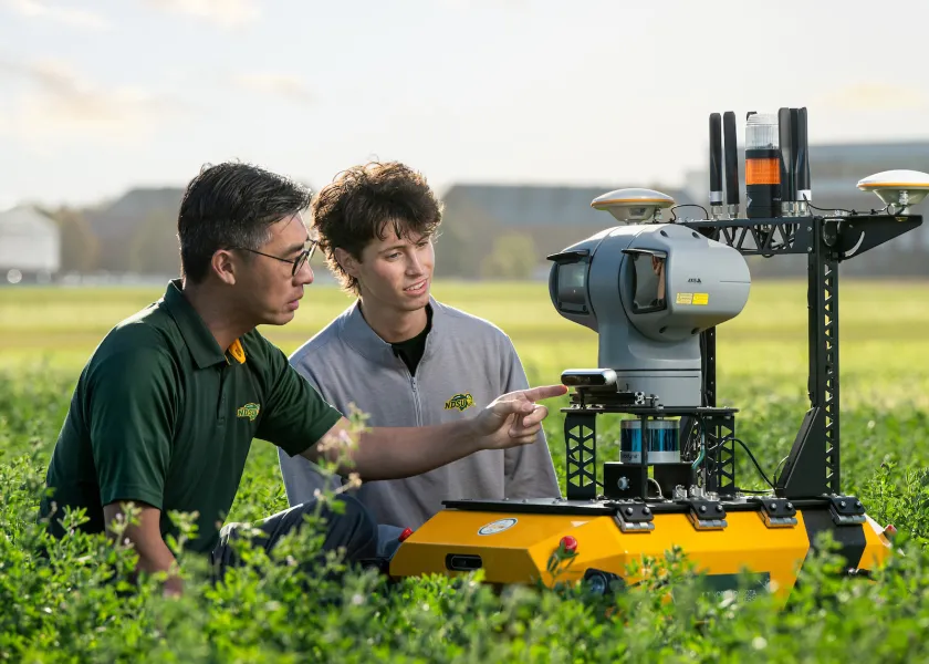 Xin (Rex) Sun and a student work with a drone in a field.
