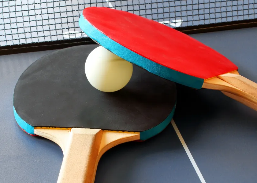Red and black table tennis paddles and white ball resting on table near net