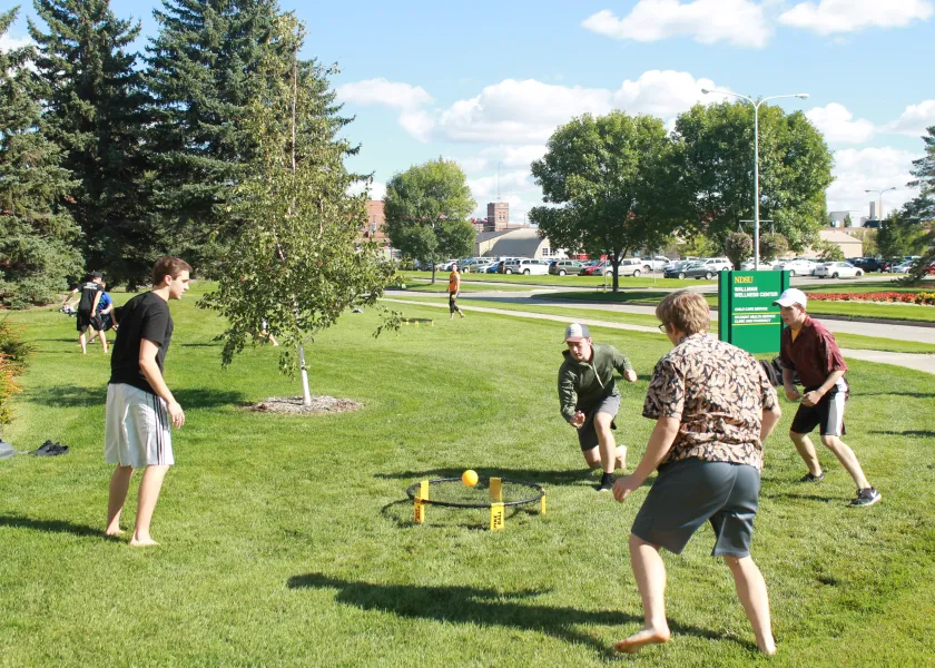 Four male students in casual clothing playing a spike ball with a yellow ball and round net
