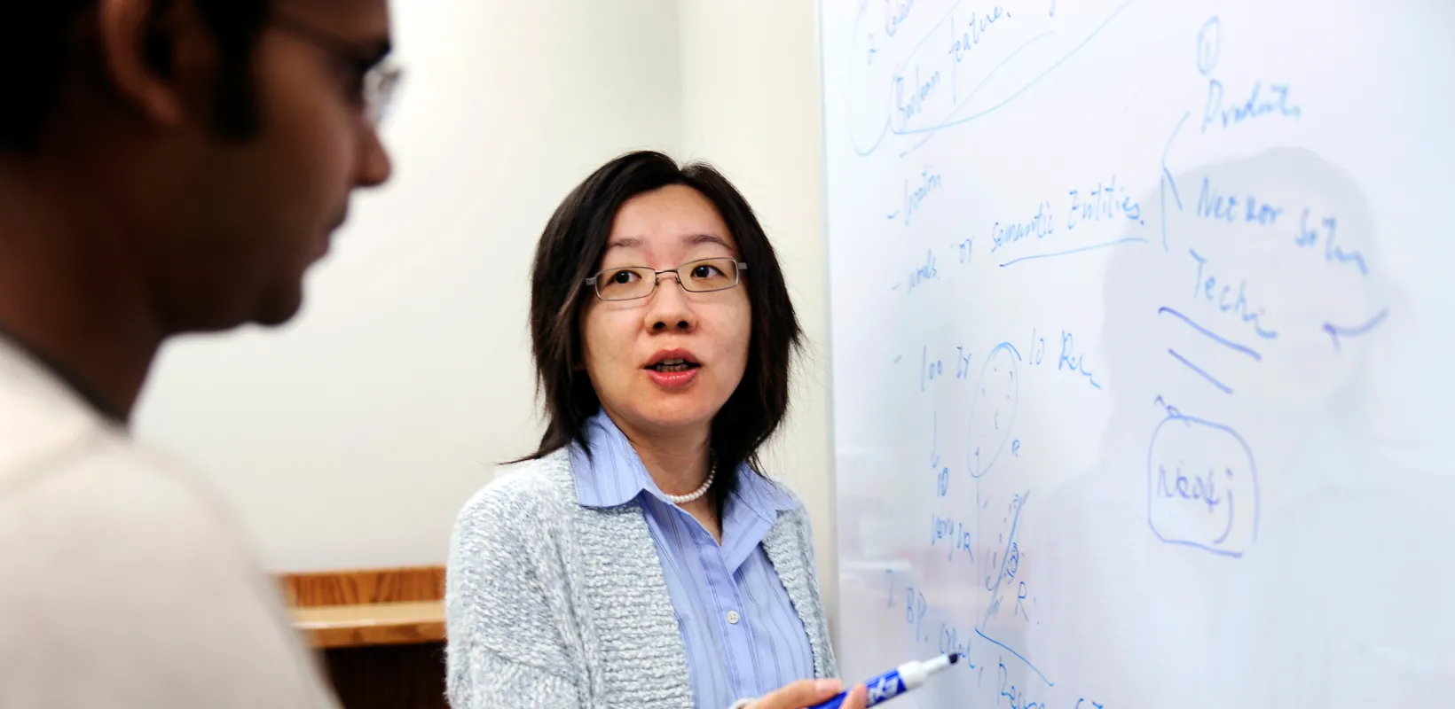 professor explaining a problem to a student at a whiteboard
