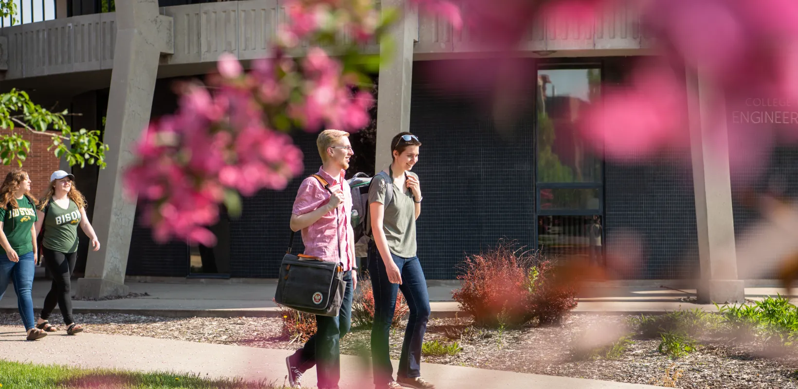 Students wearing backpacks walking on campus on a sunny day.