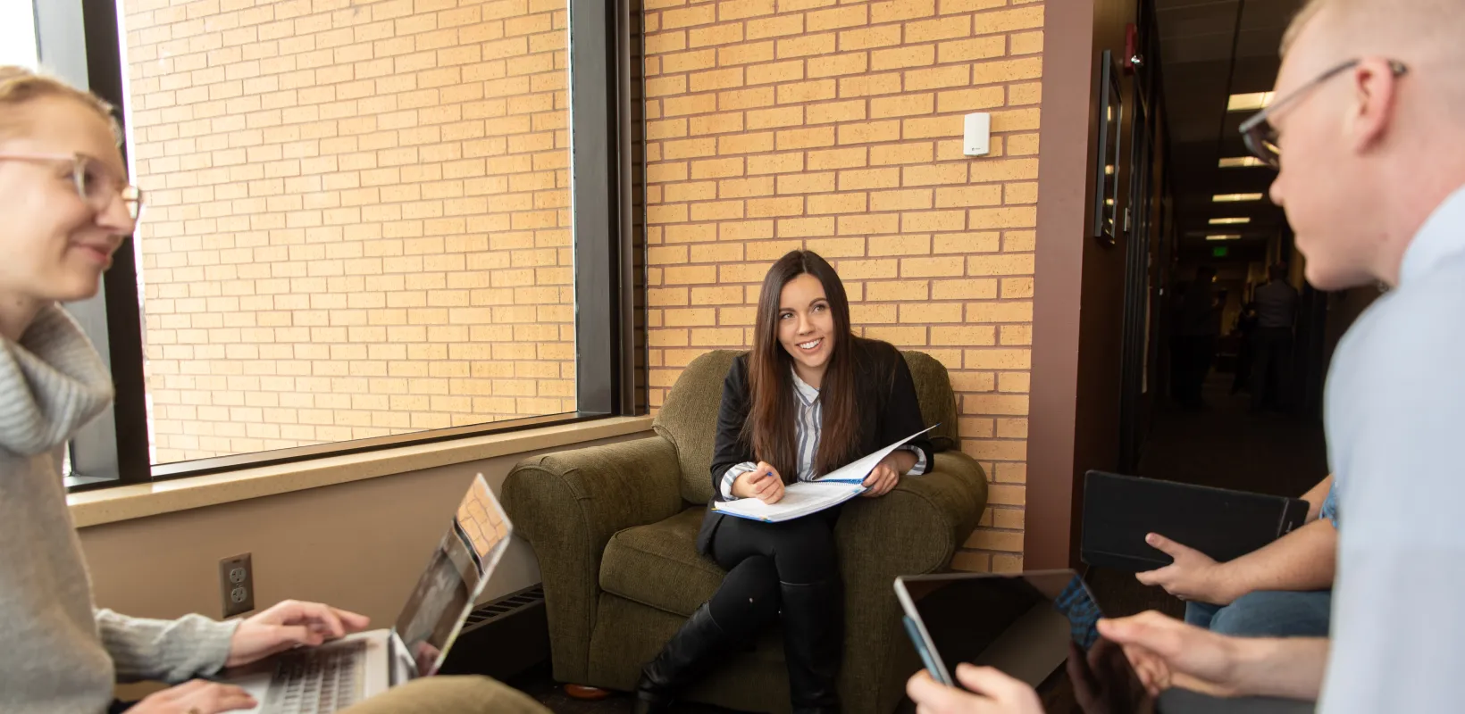 Students participating in a meeting. Some students holding a laptop, notebook or ipad.