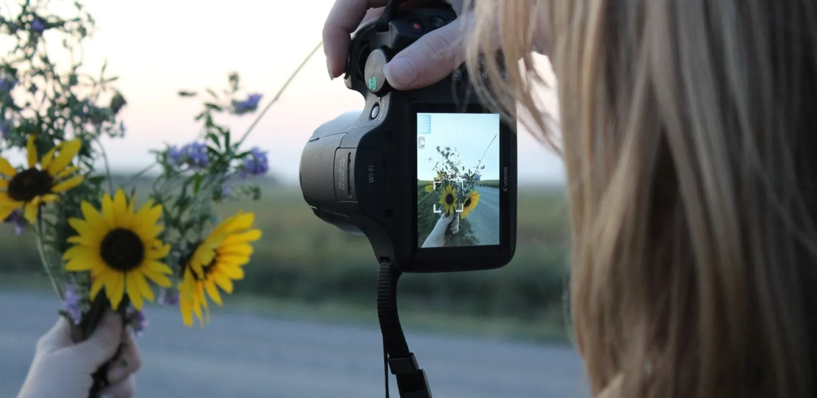 Student taking a photo of a flower bouquet containing yellow daisies and other wild flowers.