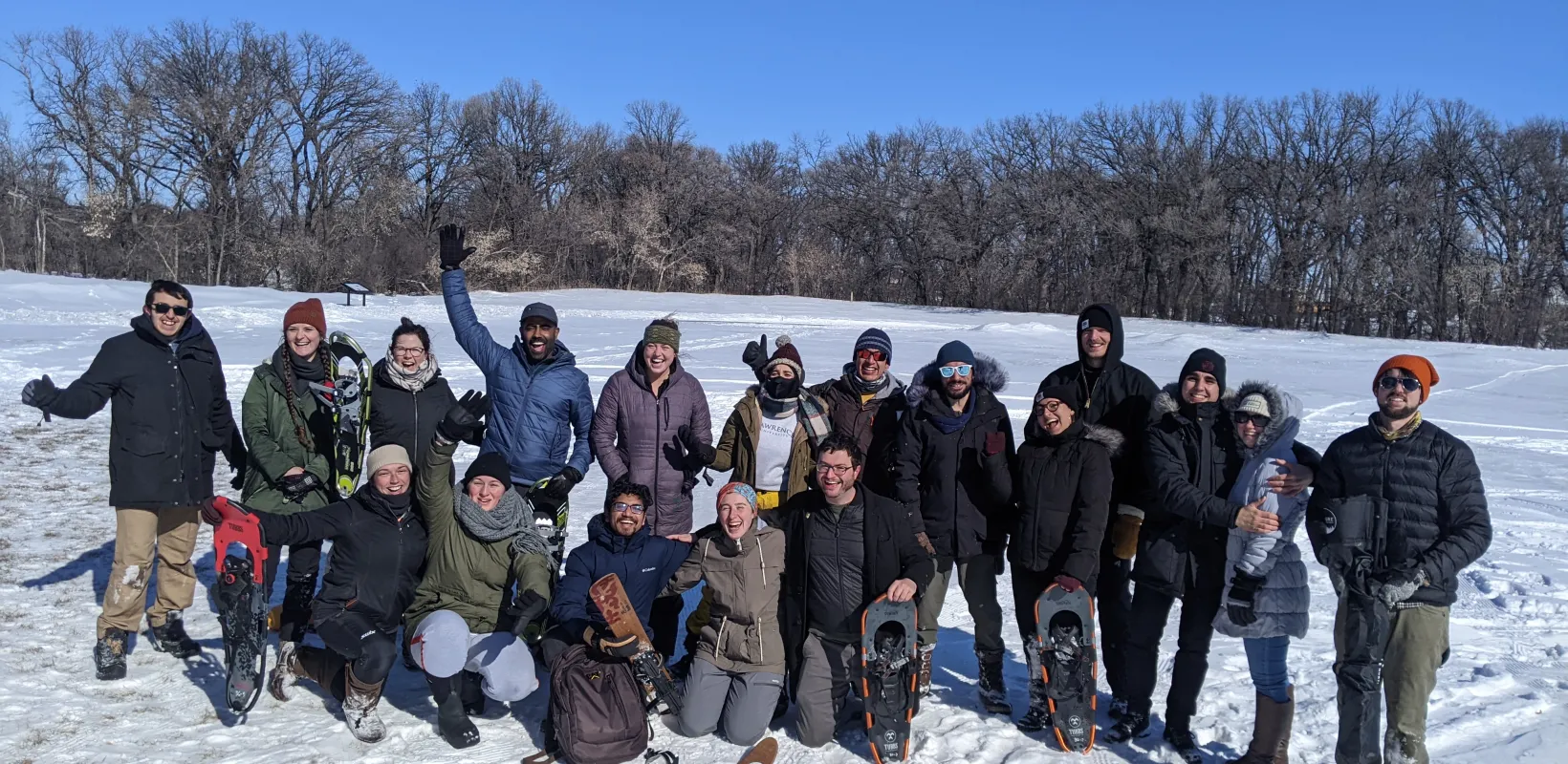 Group of students, some standing some kneeling and wearing hats, coats and snow boots, smiling confidently at camera.