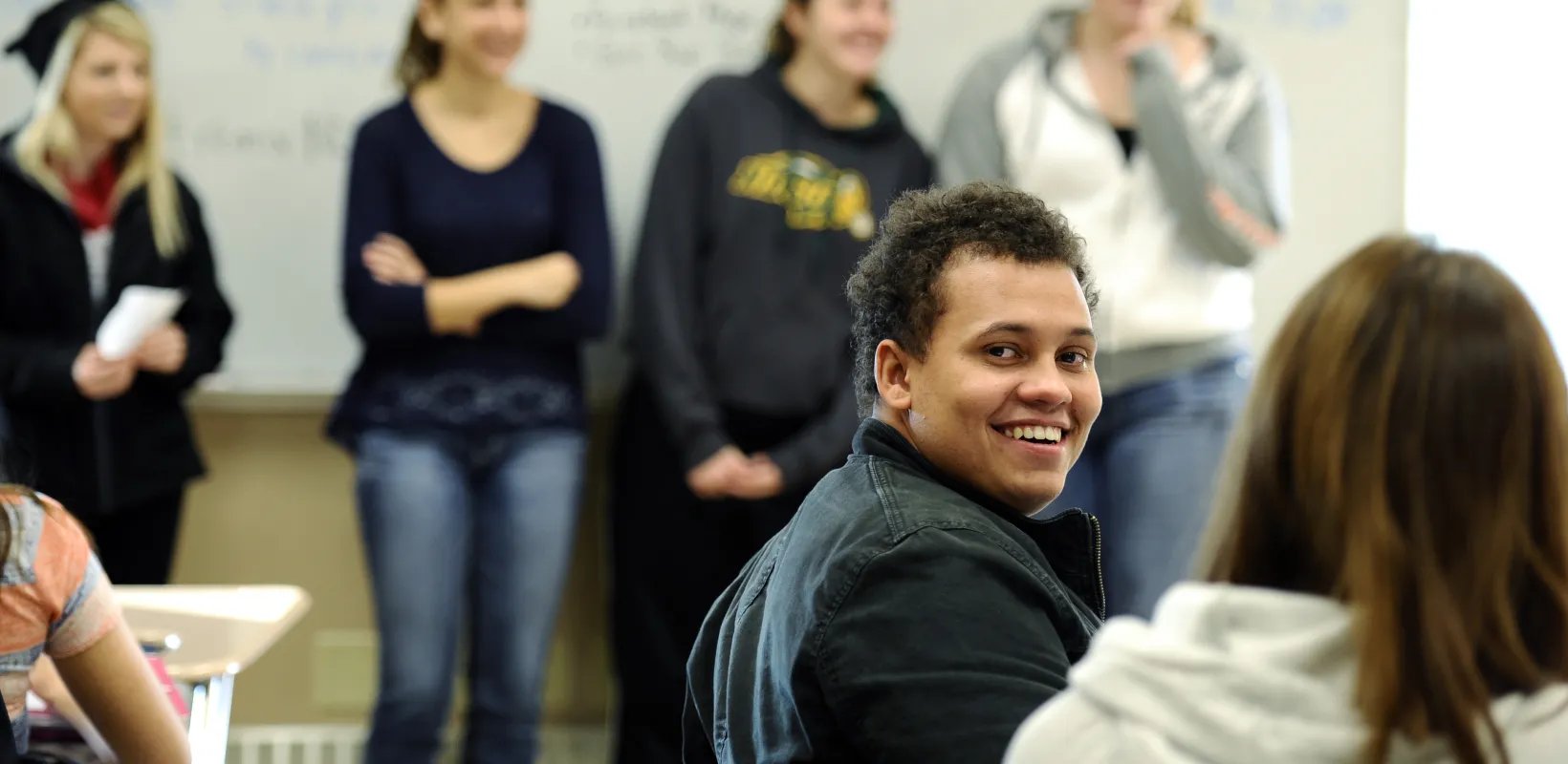 Student sitting in classroom setting looking at camera smiling