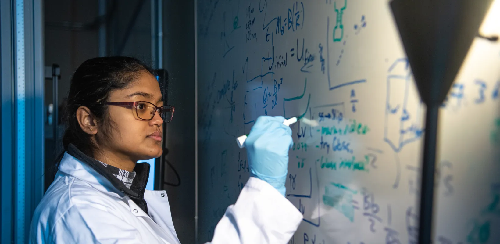 Research student working at a whiteboard. Looking intently at what she is current writing.