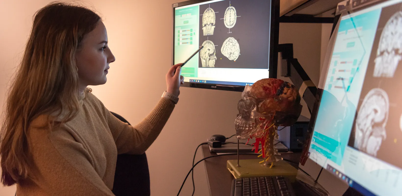 Student working at a computer in a dimly lit room. Computer screen is showing multiple pictures of a brain scan.