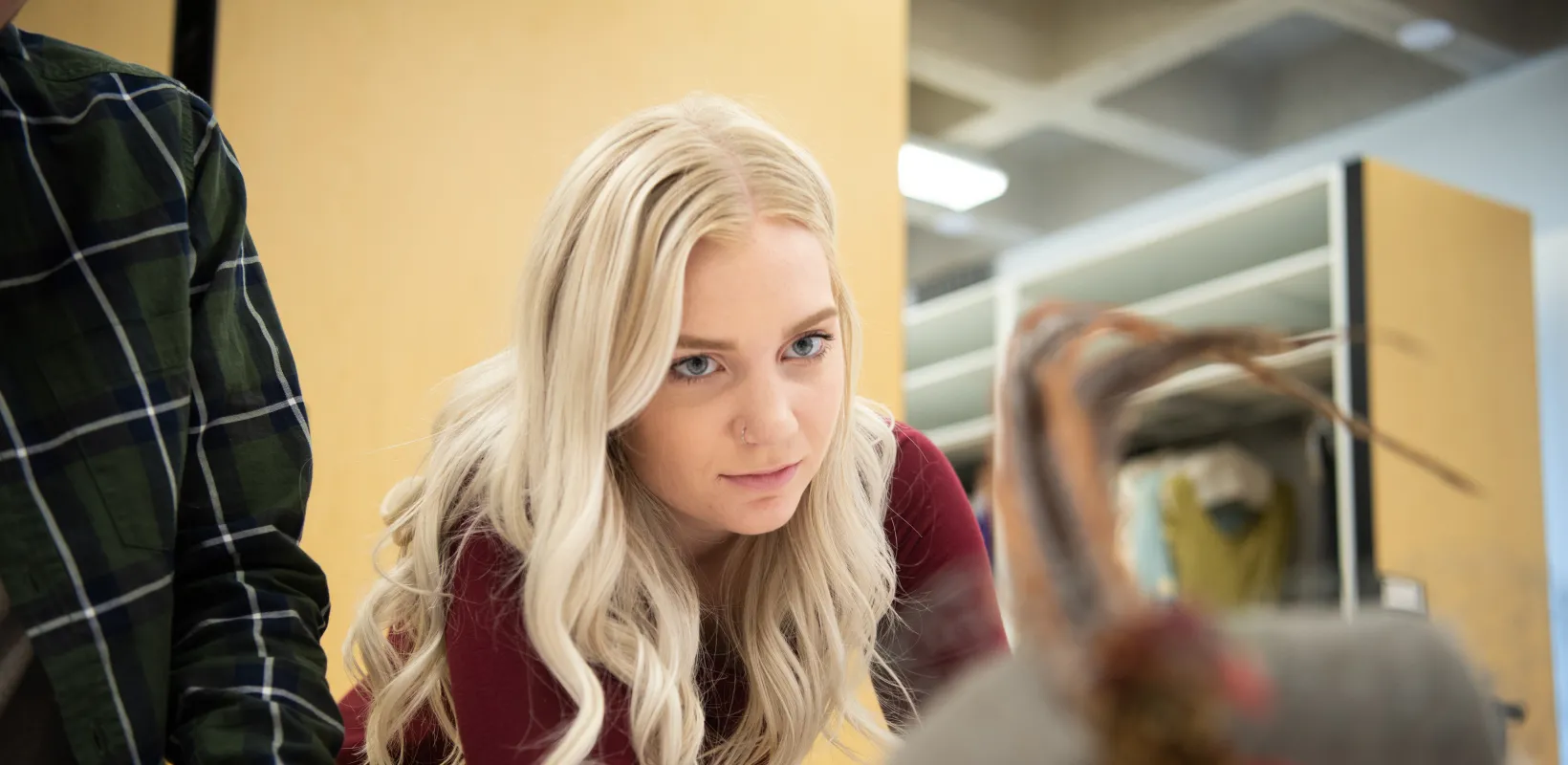 Student wearing a red sweater looking intently at a hat sitting on a table.