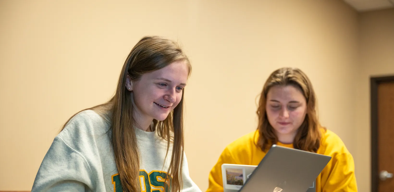 Two students working on laptops while sitting at individual desks.