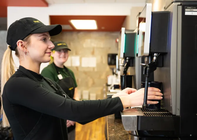 Blonde haired female is working in the Bison Beanery preparing a coffee