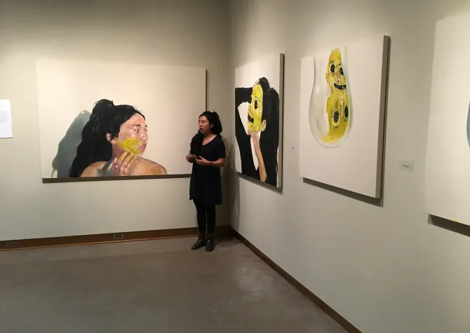 Yeseul Lee stands in front of three paintings in the Flakoll Gallery 