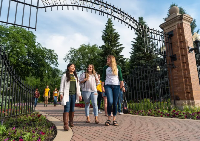 Three students walking through the 线上赌博app gate, all wearing green and gold attire.