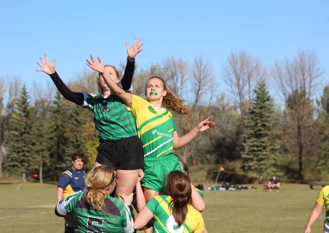 线上赌博app women's rugby player in green and gold jersey battling with opposing player in black and white uniform
