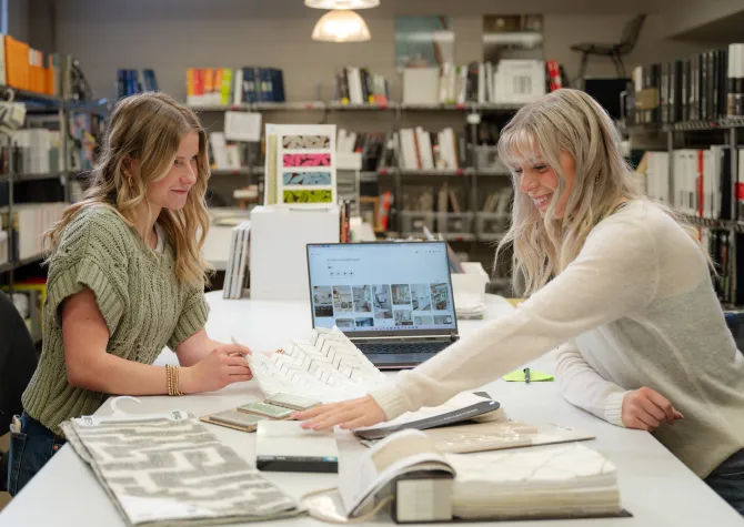 Students working in design studio with fabric and tile samples and laptop computer.
