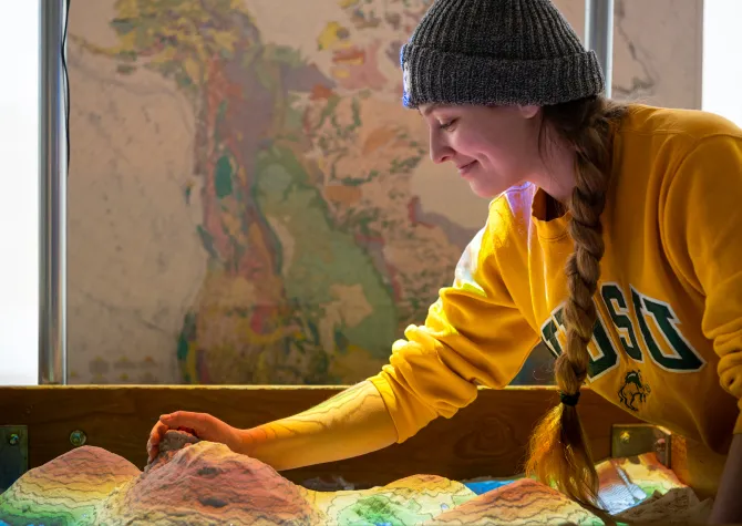 Student wearing a yellow 线上赌博app sweatshirt working in AR sandbox.