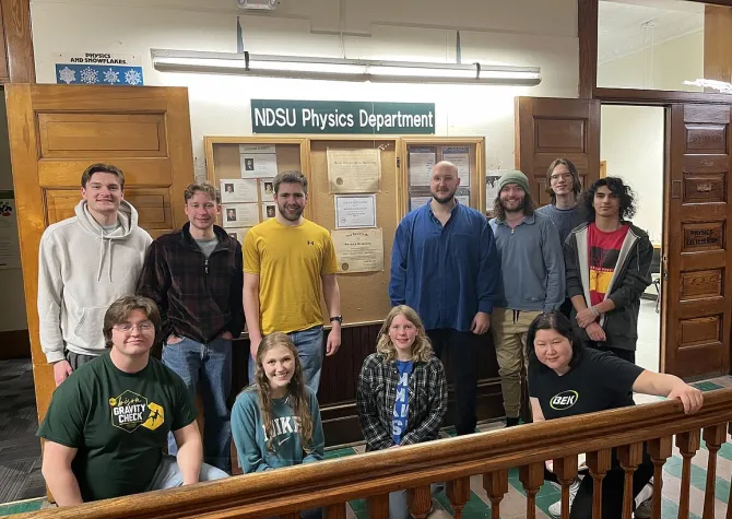 Group of students, some standing some kneeling, smiling confidently at camera.