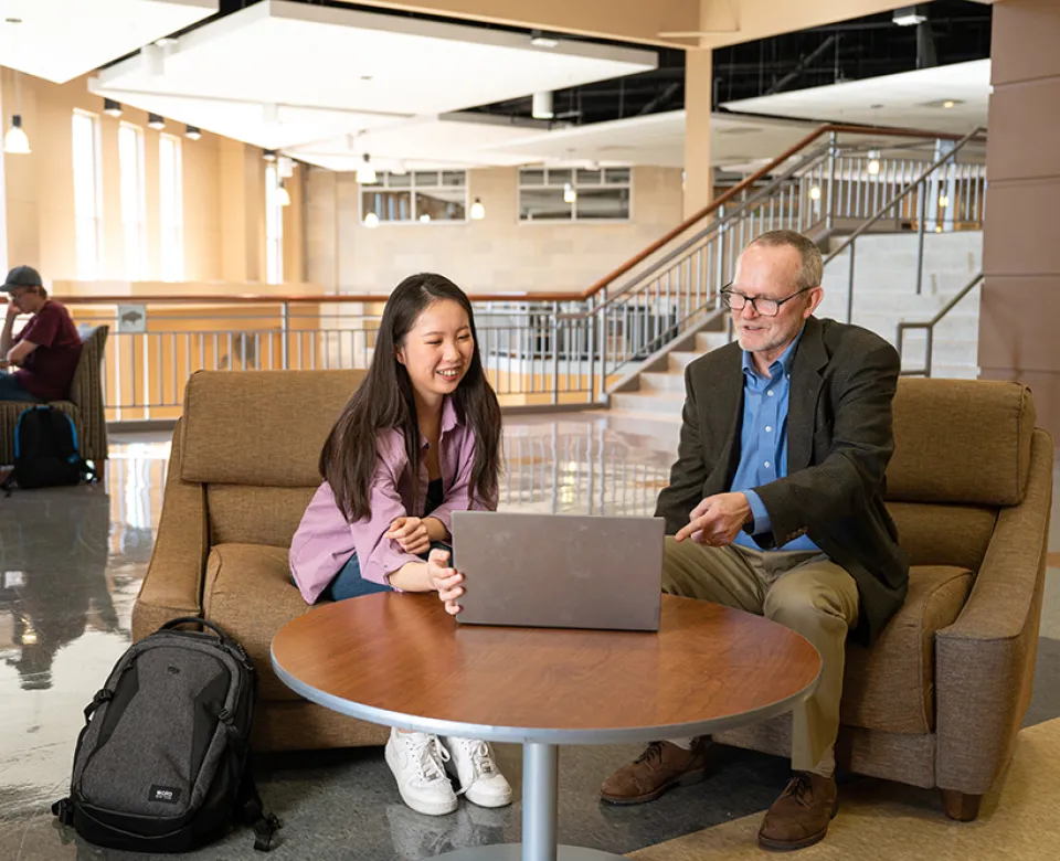 Student showing work to instructor on laptop in Barry Hall study area.