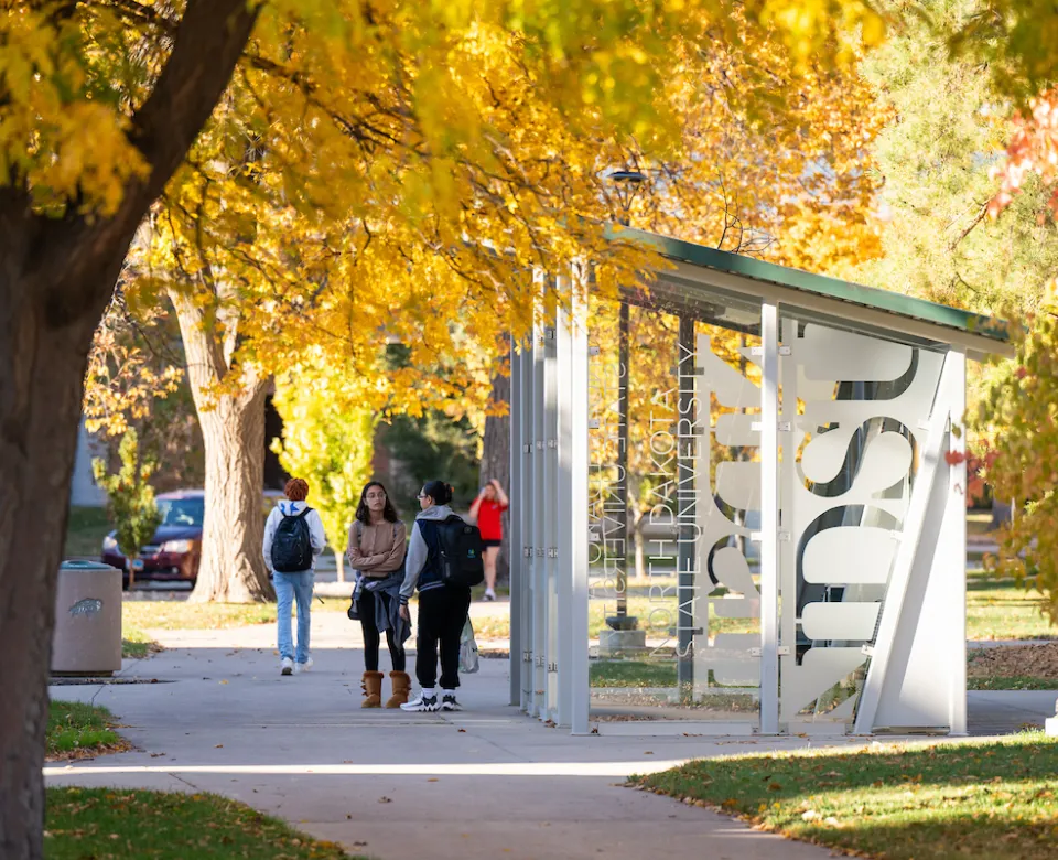 students waiting by bus shelter on campus on a fall day