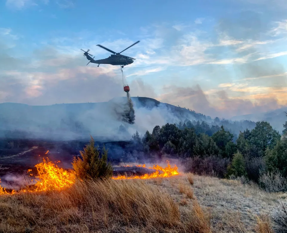 A Blackhawk helicopter drops water onto a fire burning near a forest
