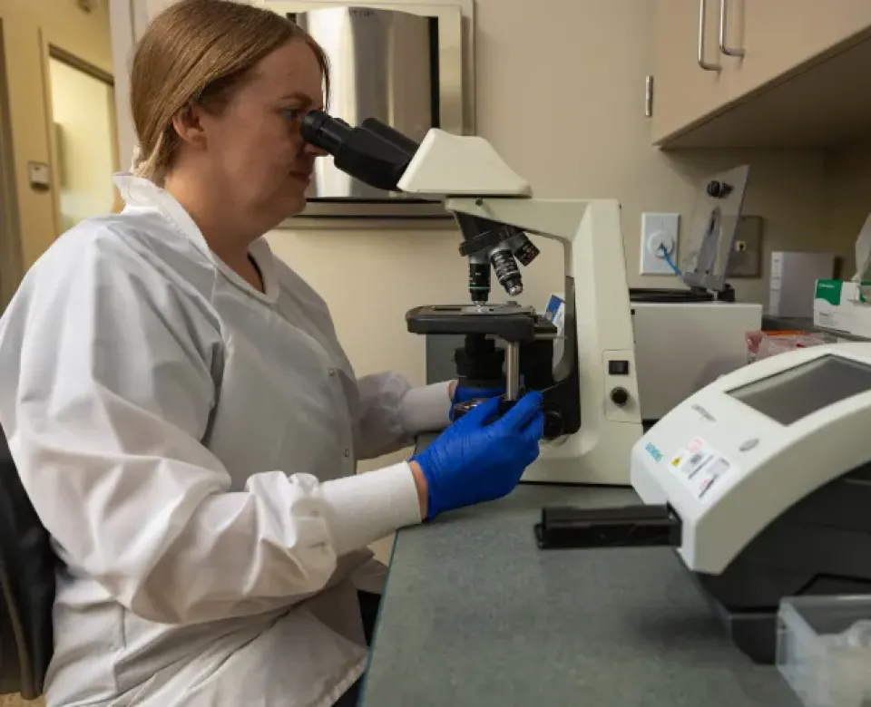 Medical lab worker looking into microscope.