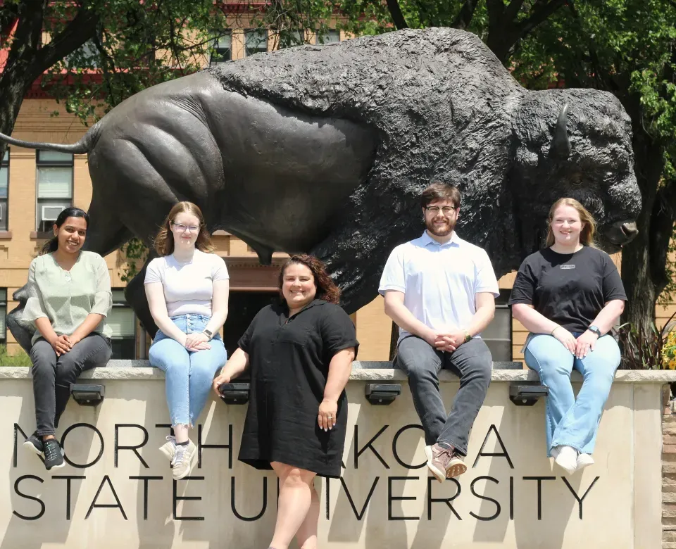 5 GBGSA officers posing in front of the bronze Bison smiling confidently at camera.