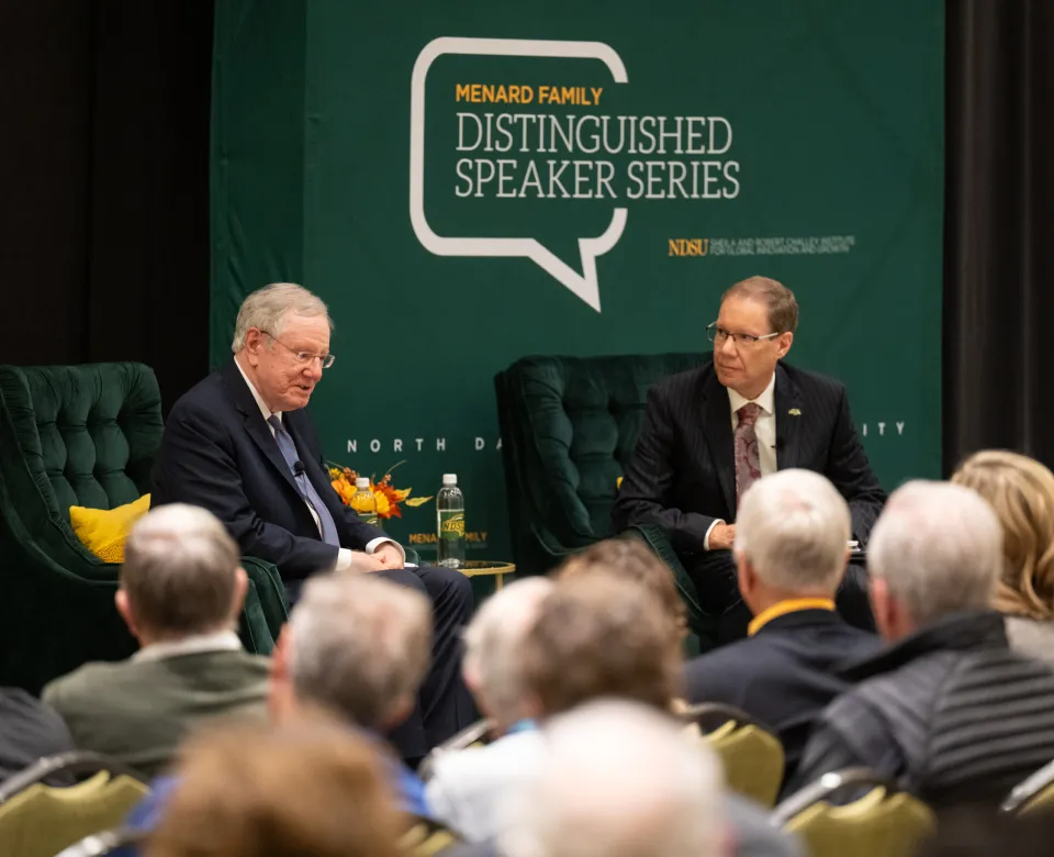 John Bitzan and Steve Forbes on stage at an event.
