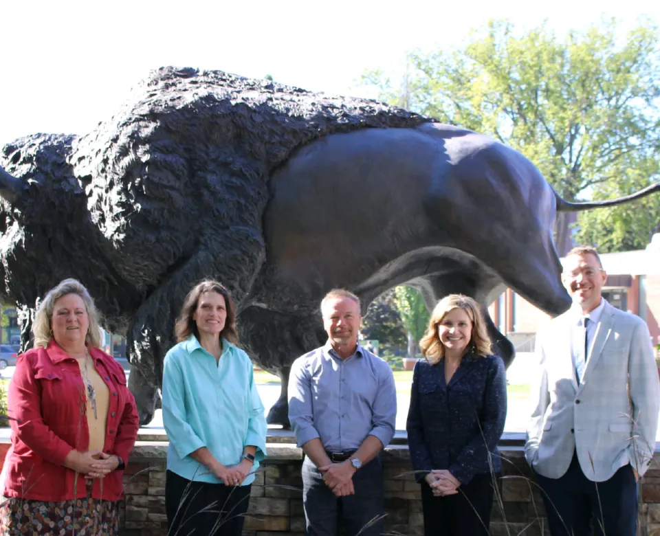 Faculty standing in front of the Bison statue smiling confidently at the camera