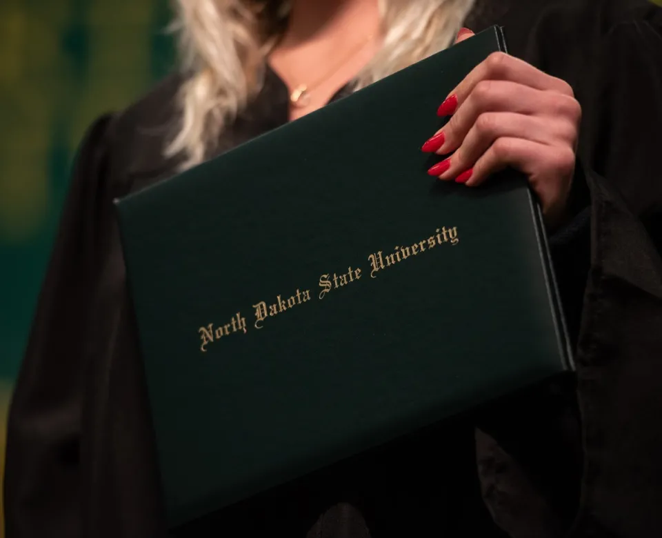 Student holding a North Dakota State degree that is green with gold lettering.