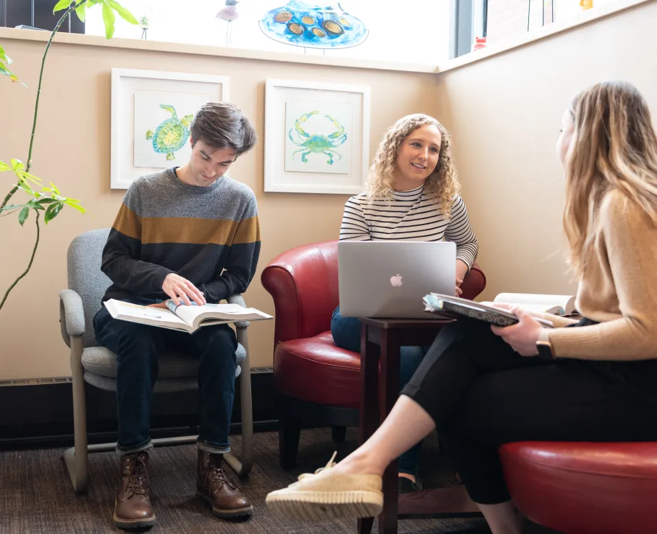 Student sitting on chairs while visiting. Once student has a laptop sitting on her legs and the other students have books and or notebooks on their laps. 