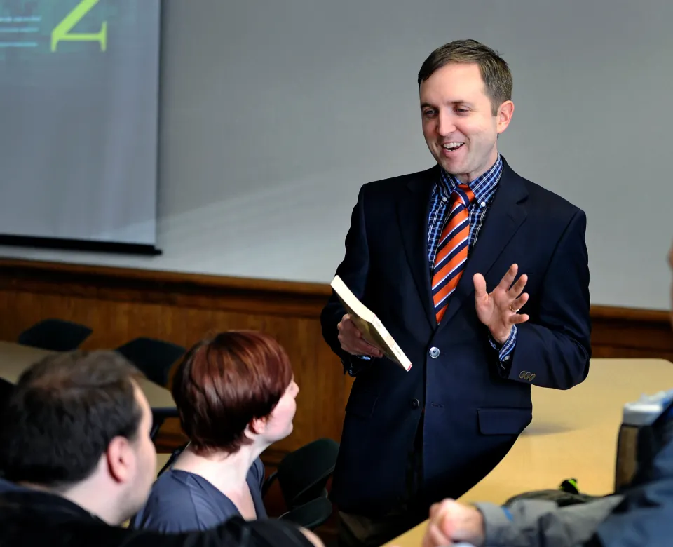 Dr. Beck holding a book and speaking to a group of students.
