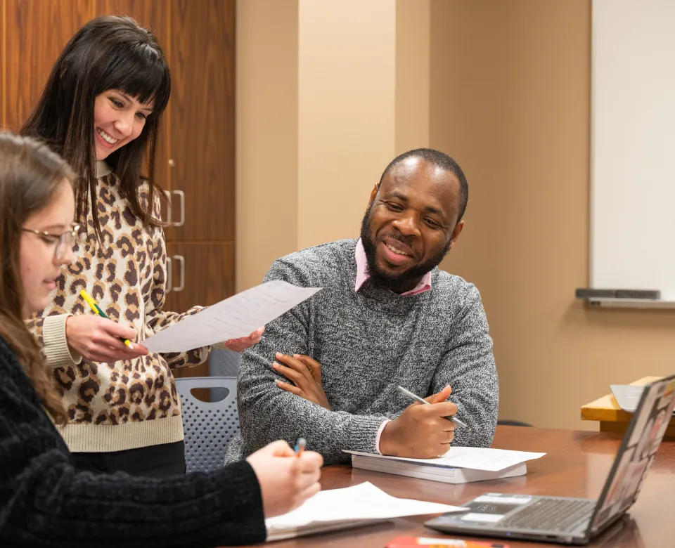Students working together at desk with pen, paper and a laptop.